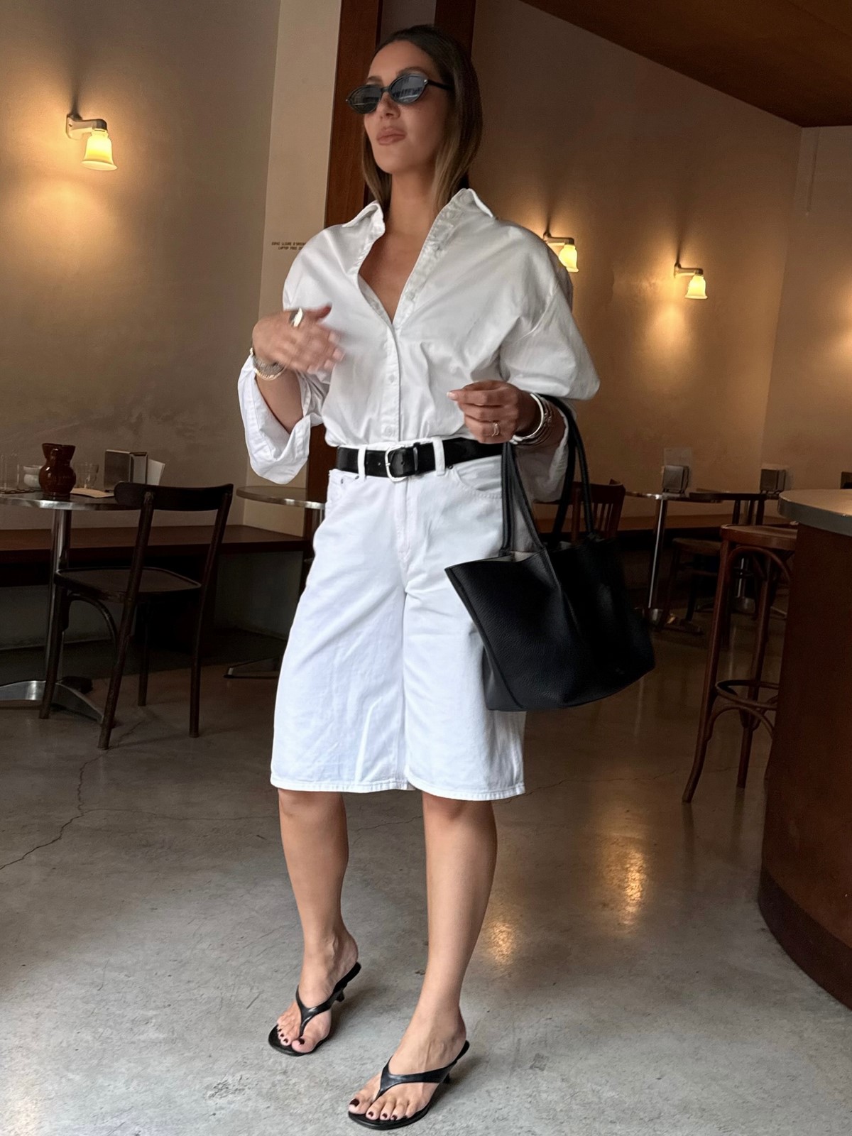 Білі бермуди з об’ємною сорочкою, чорним ременем і великою сумкою