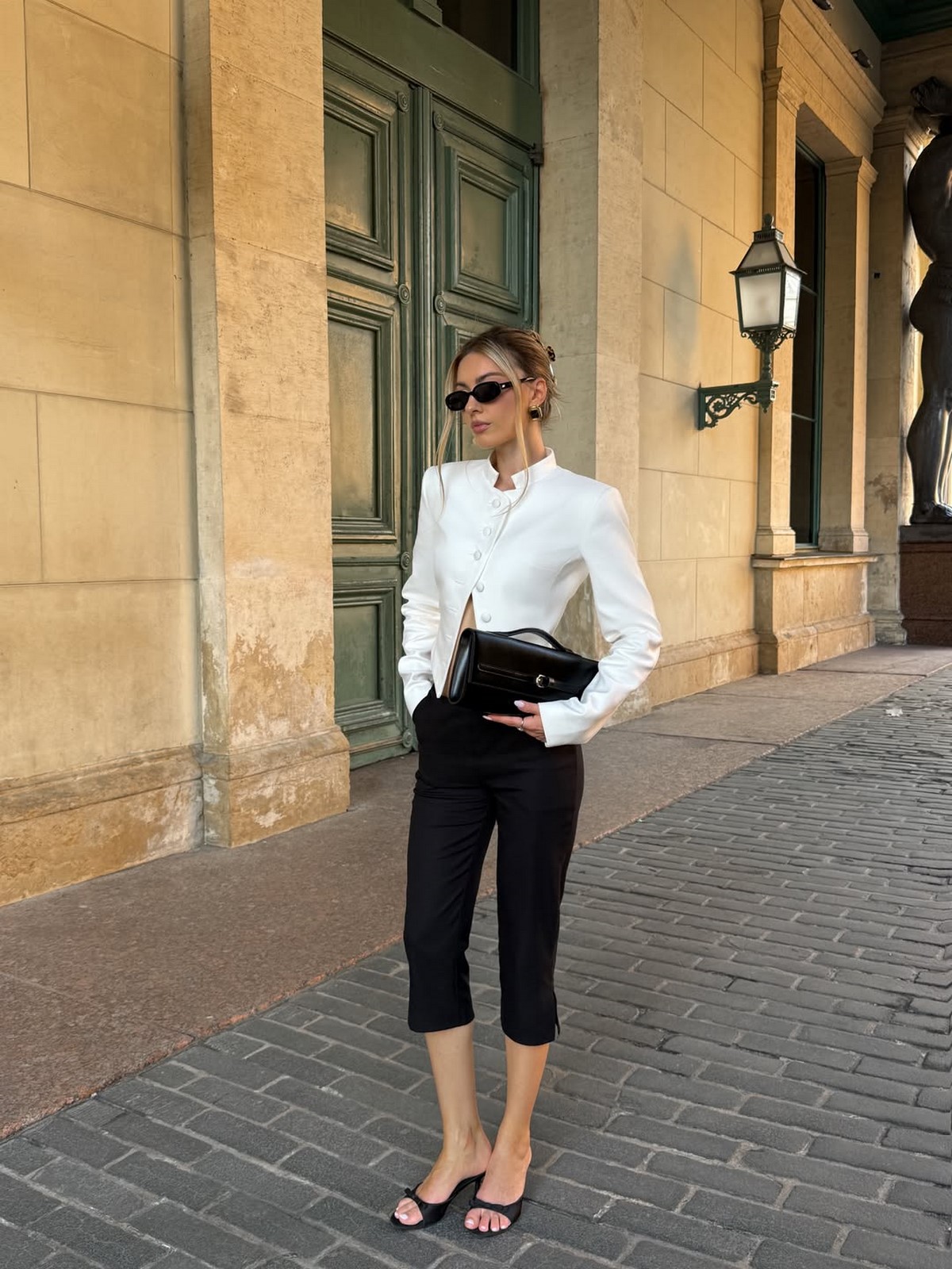 Чорні капрі, білий жакет і чорні мюлі kitten heels на міській вулиці
