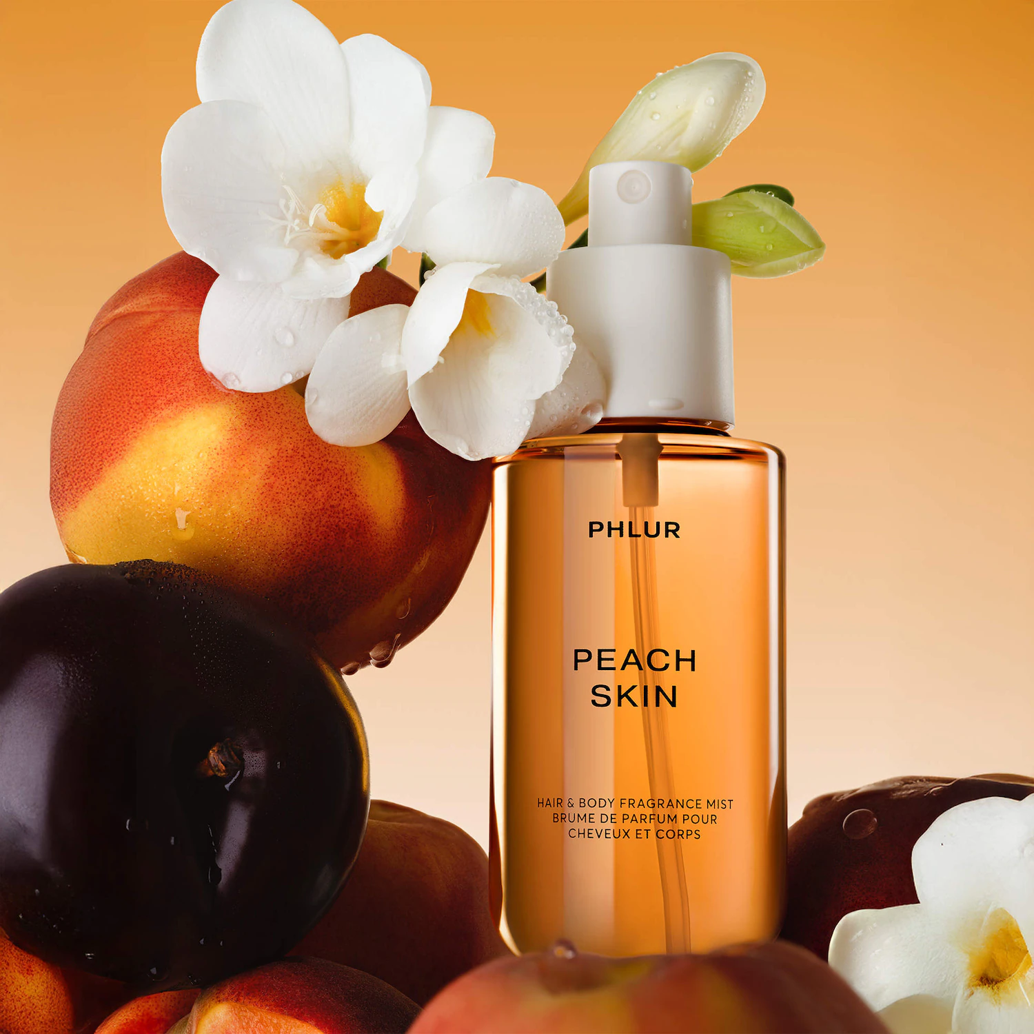 Флакон PHLUR Peach Skin Hair & Body Fragrance Mist на тлі персиків, темних фруктів і білих квітів