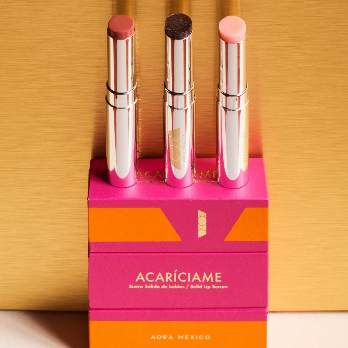 AORA ACARÍCIAME Solid Lip Serum у металевому пакуванні на яскравій рожево-помаранчевій коробці