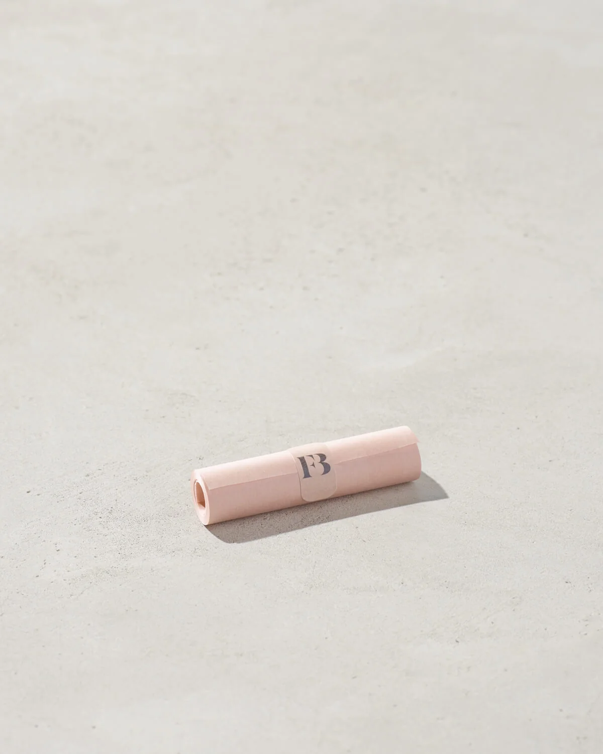 Стік-бальзам FB (Fenty Beauty), загорнутий у рожевий папір, лежить на бетонній поверхні