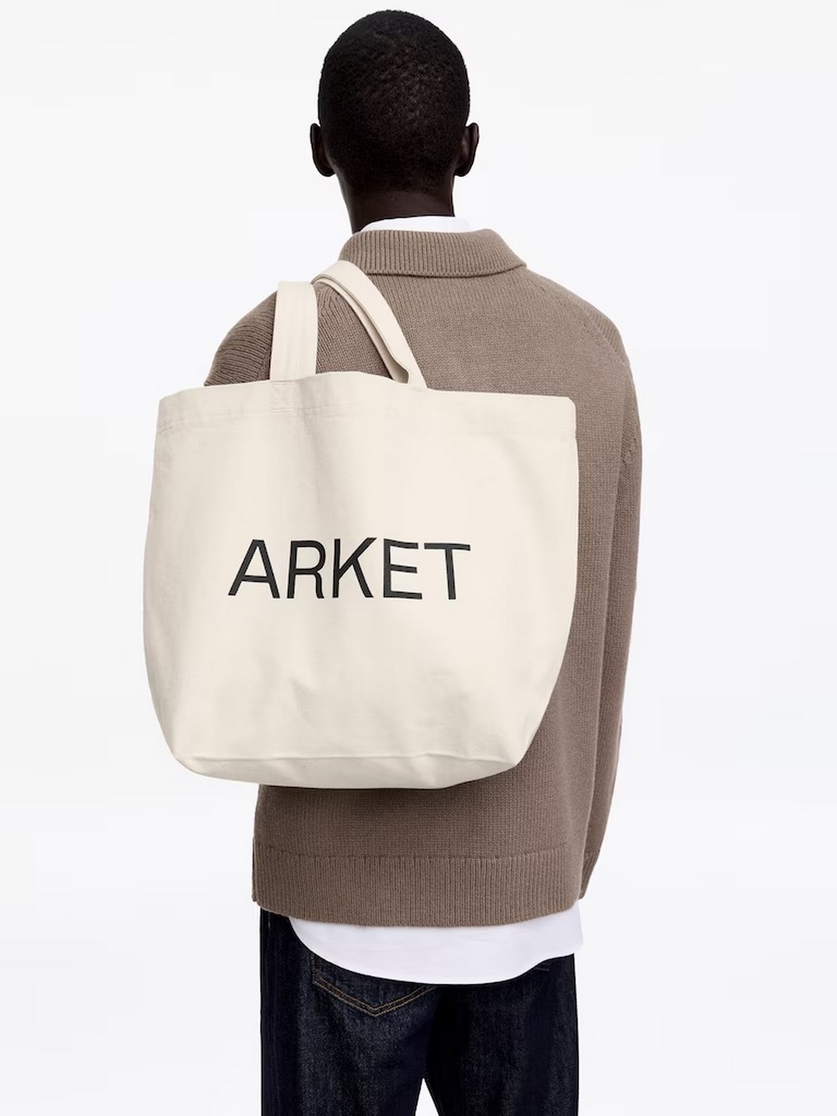 Чоловік несе на плечі великий молочний текстильний тоут ARKET